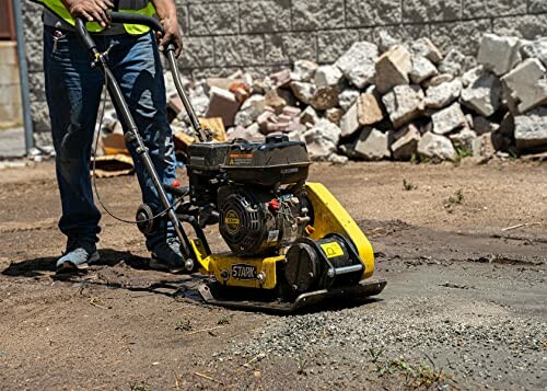 Worker operating a yellow plate compactor on a construction site.